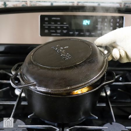 A hand in an oven mitt lifting the lid of Lodge Cast Iron Double Dutch Oven containing food