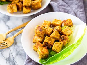 Cubed fried tofu on a plate with a leaf of romaine lettuce