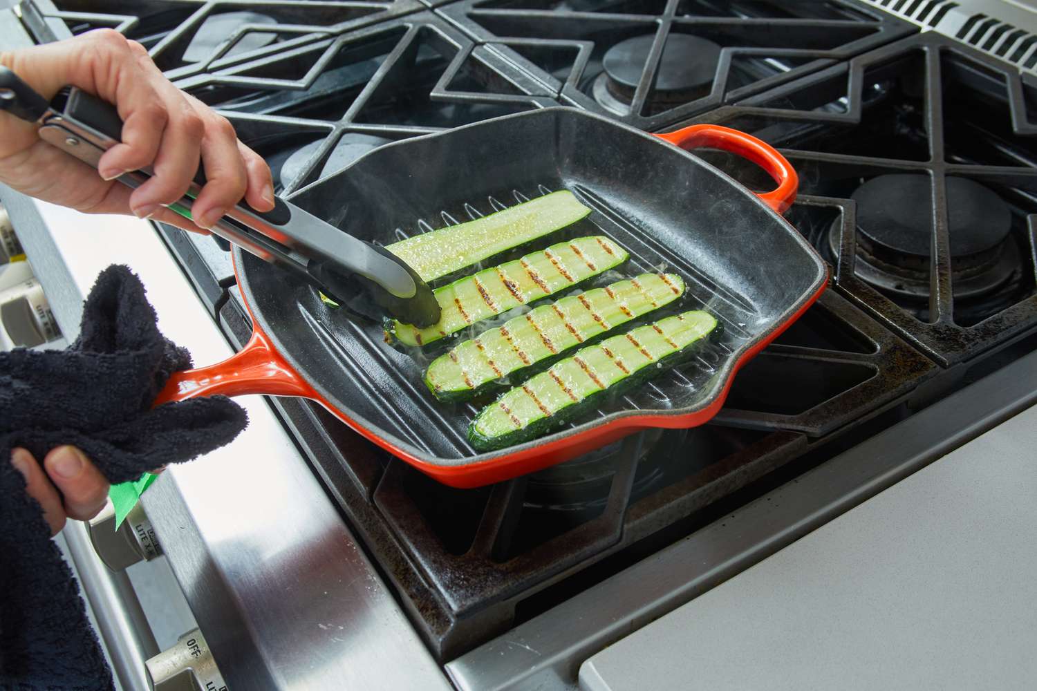 A person flipping zucchinis being grilled in the Le Creuset Square Skillet Grill Pan.