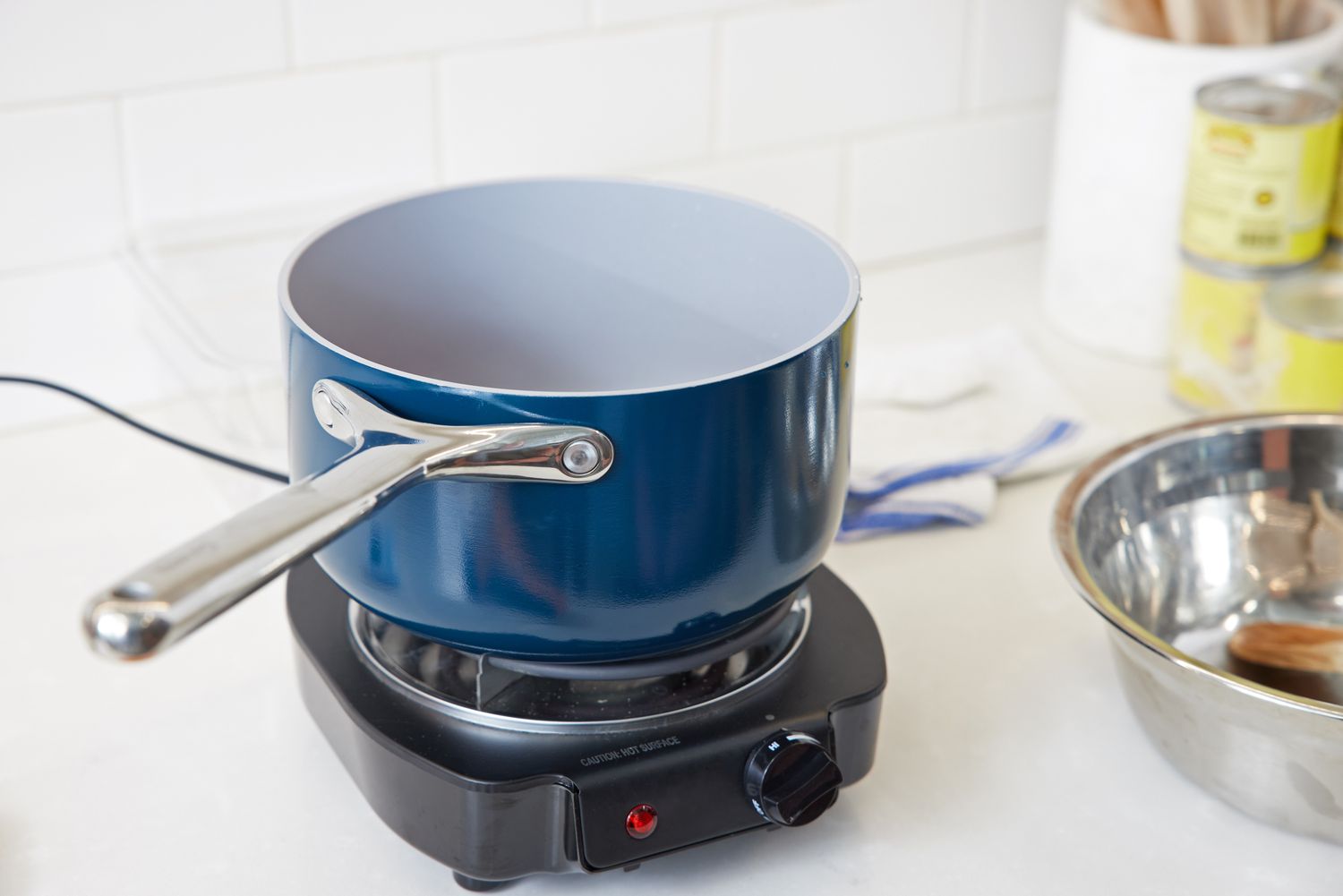 A blue Caraway sauce pan on a hotplate.