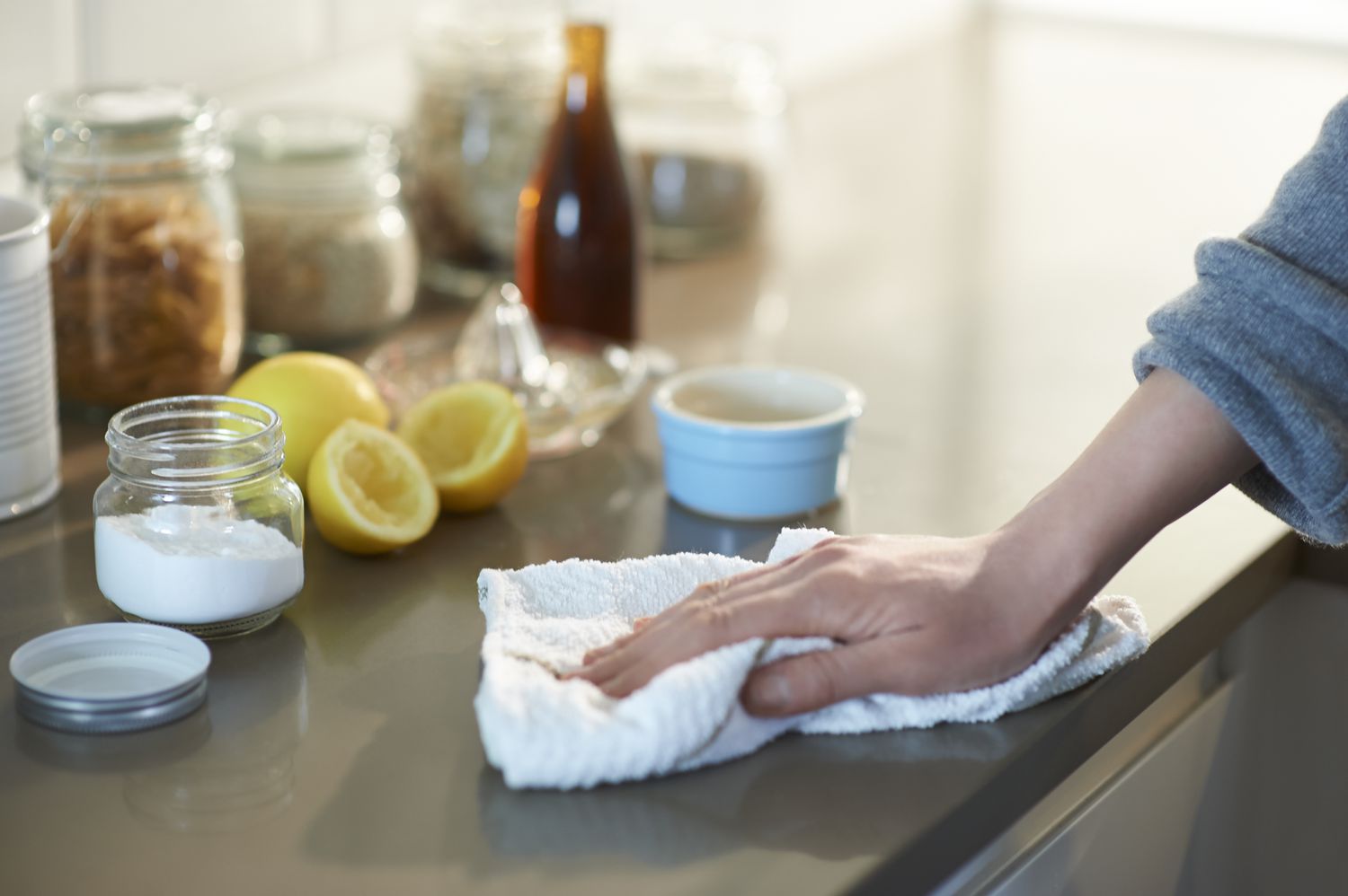 Person cleaning countertops with a cloth next to a container filled with baking soda and some lemons.