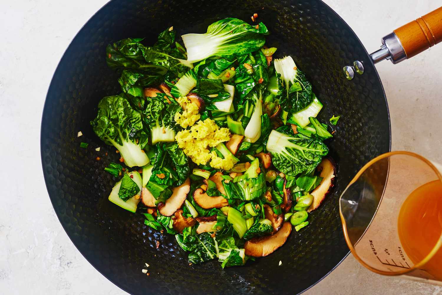 Broth added to bok choy and shiitake mushroom stir fry cooking in a wok 