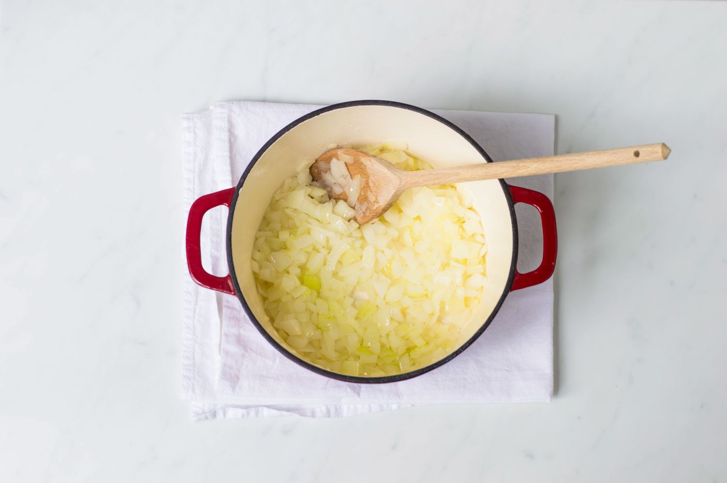 Onions cooking in a Dutch oven with a wooden spoon