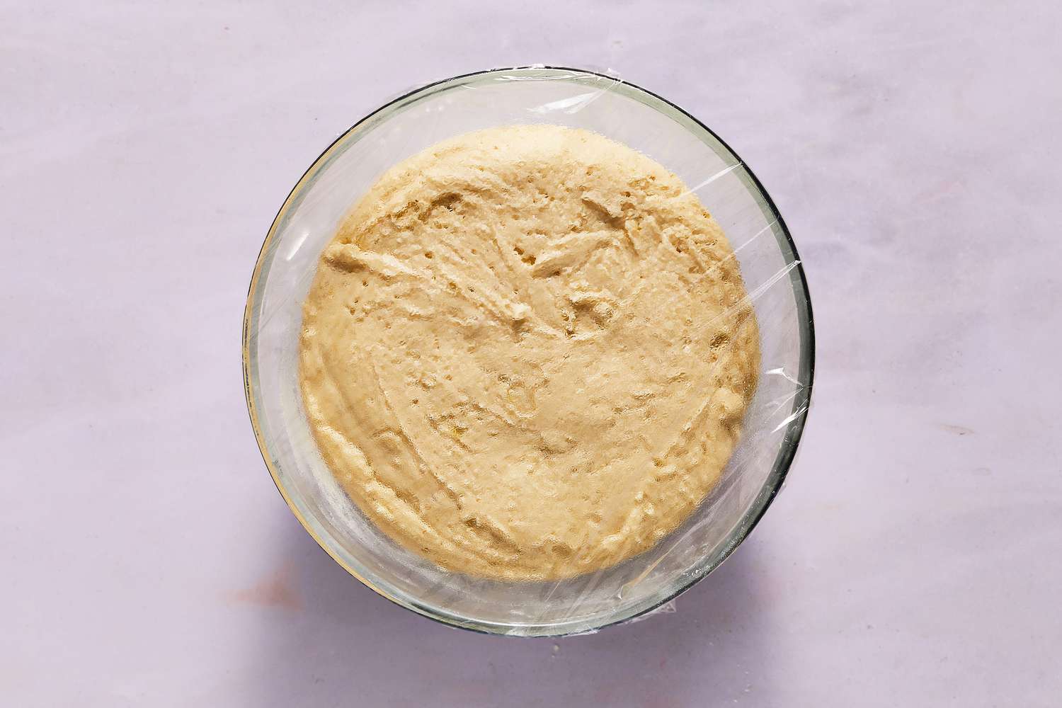 gluten free focaccia dough in bowl covered with plastic wrap after a rise