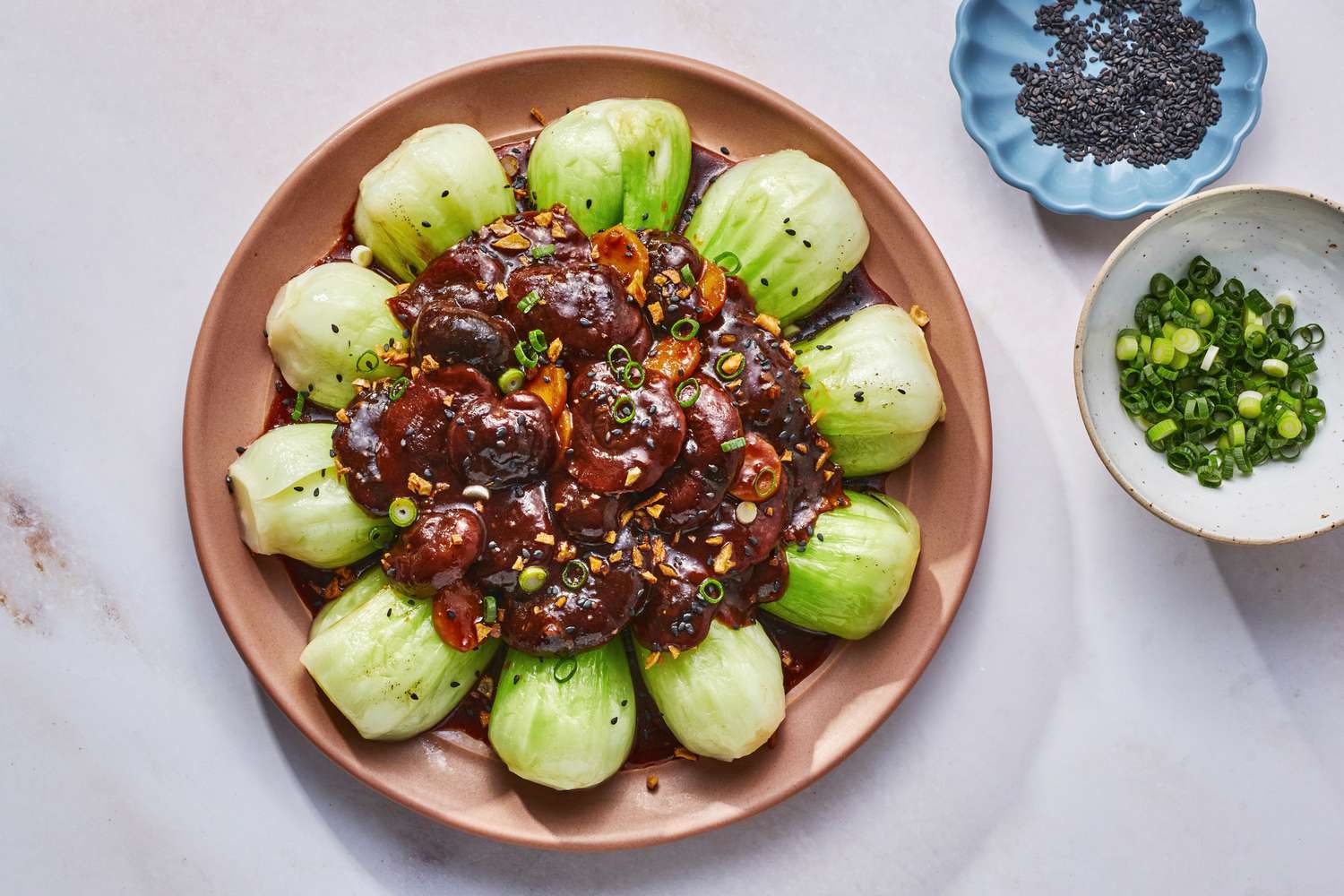 A platter of braised shiitake mushrooms served on a ring of cooked baby bok choy, garnished with fried garlic, sesame seeds, and sliced scallions