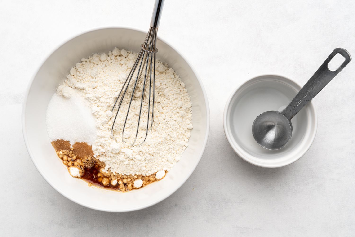 Pancake mix, sugar, and vanilla extract combined in a large bowl and water being added by the tablespoon