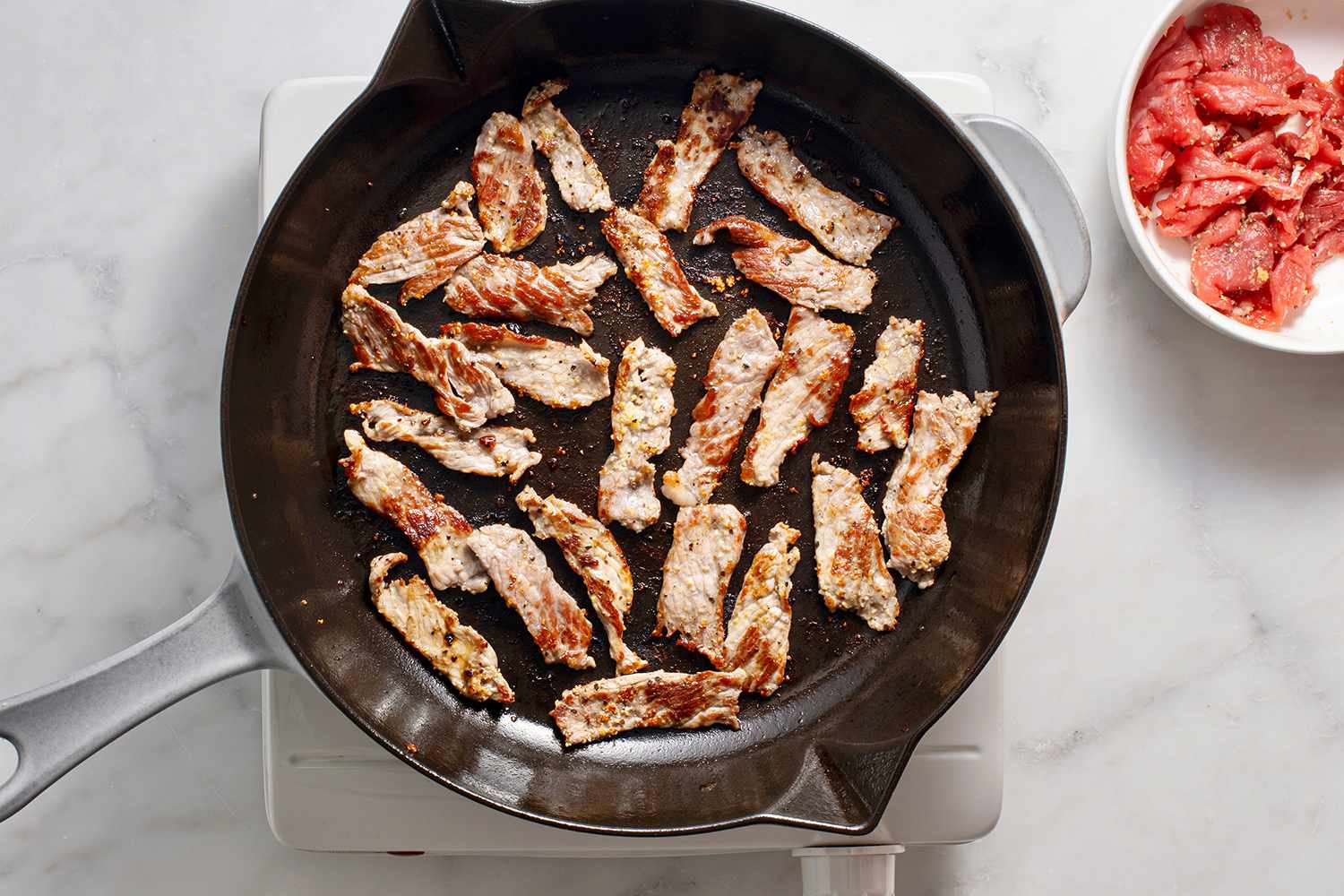 Slices of steak cooking in a single layer in a pan