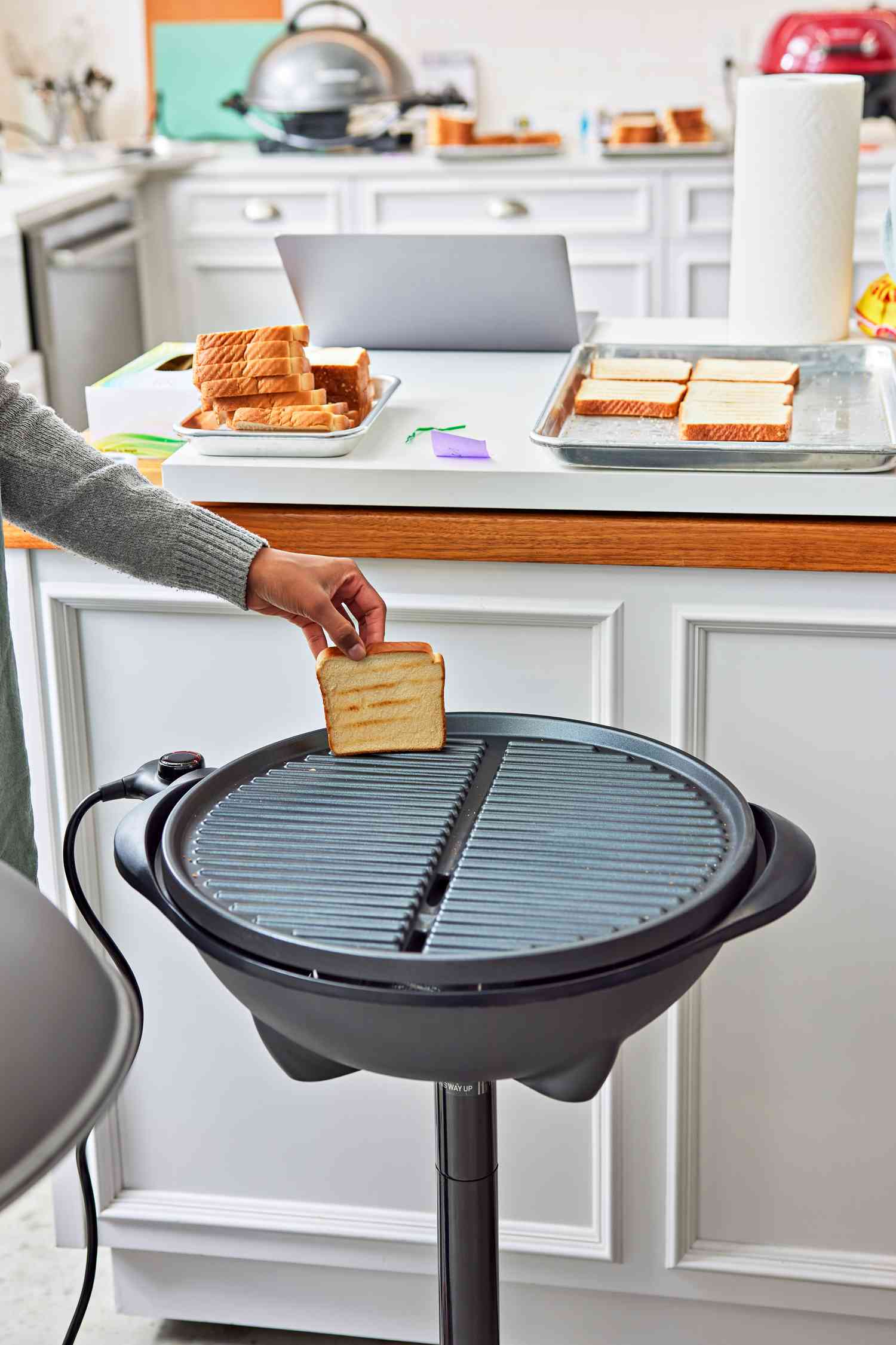 Hand placing a slice of bread onto the George Foreman GFO240S Indoor/Outdoor Electric Grill in a text kitchen 