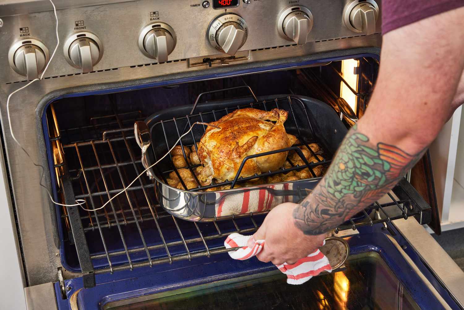Hand pulling the All-Clad Stainless Steel Nonstick Roasting Pan With Rack with a chicken from the oven