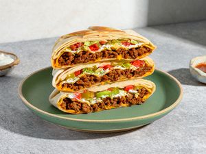 A plate of stacked Crunchwrap Supremes, cut in half, served with salsa and sour cream