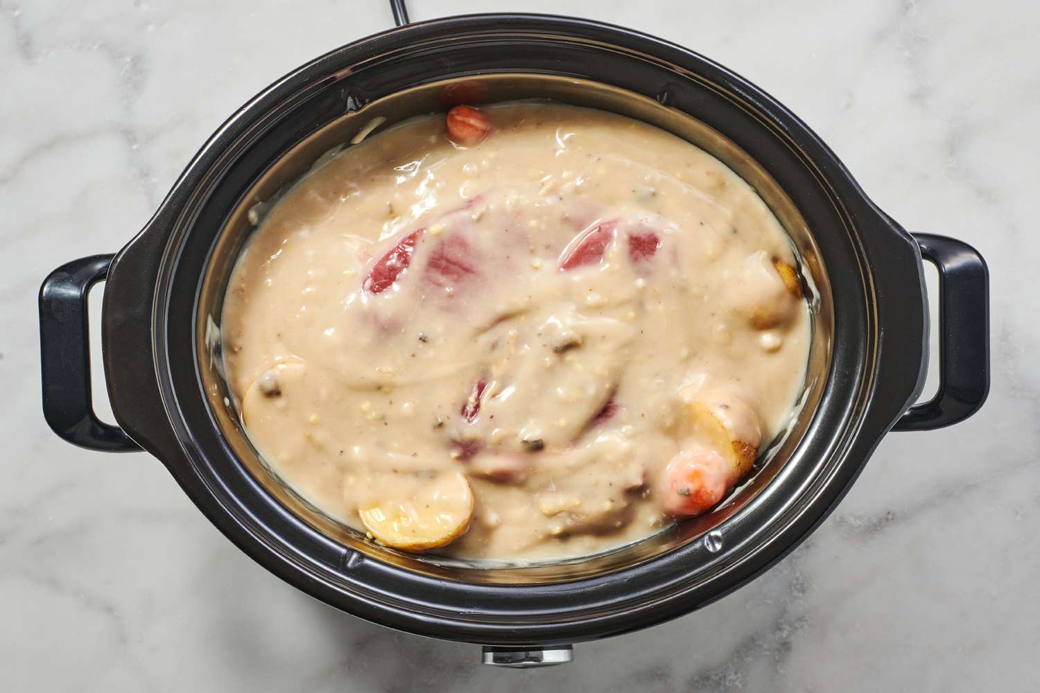 A slow cooker with a pot roast, carrots, and potatoes covered with mushroom-onion soup mix mixture