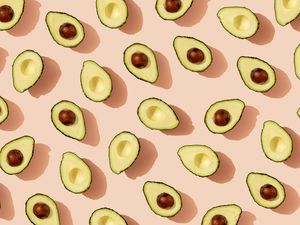 Many halved avocados sitting face-up on a light pink surface