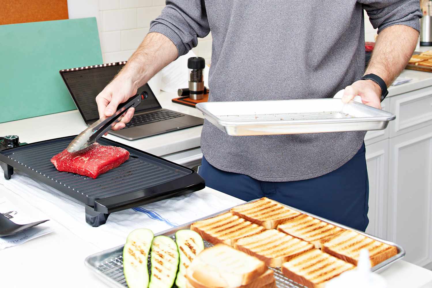 Man using tongs to cook steak on the Presto 09020 Cool Touch Electric Indoor Grill