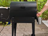 Hand lifting a small bucket from the side of a Traeger TFB30KLF Tailgater Pellet Grill