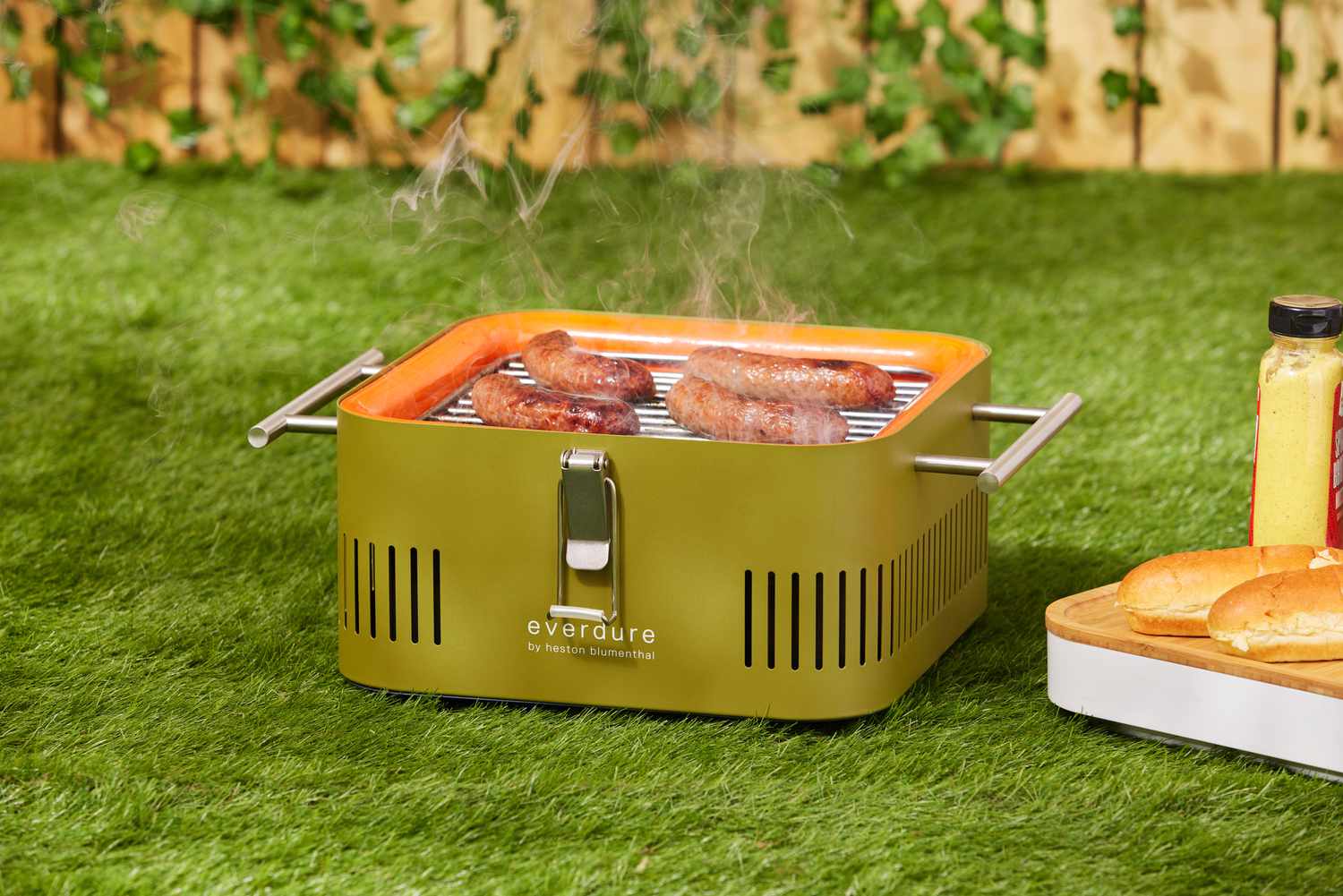 Sausage grilling on Everdure Cube Portable Charcoal Grill displayed on grass