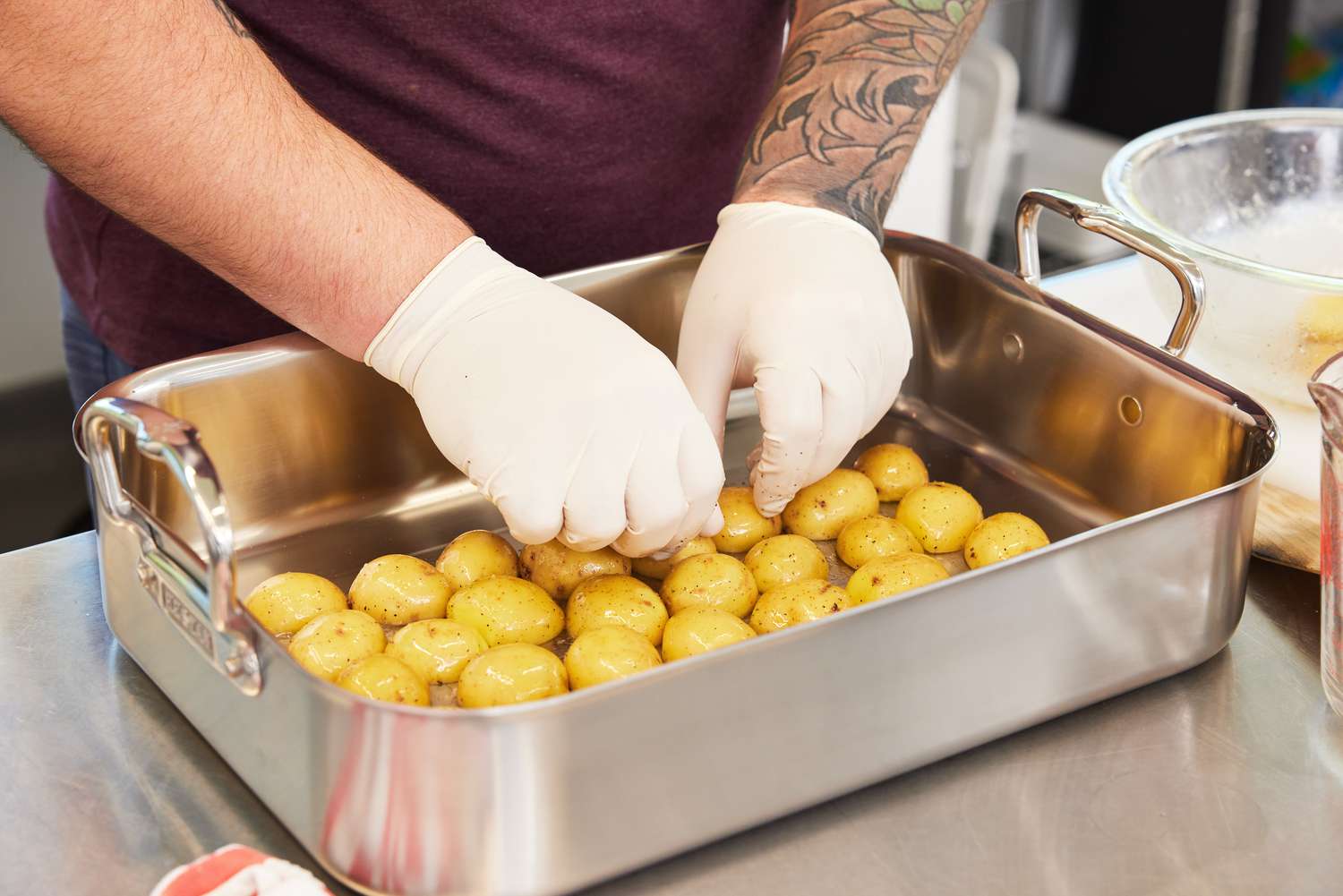 Hands grabbing potatoes in the Hestan Provisions Stainless Steel Classic Roaster with Rack