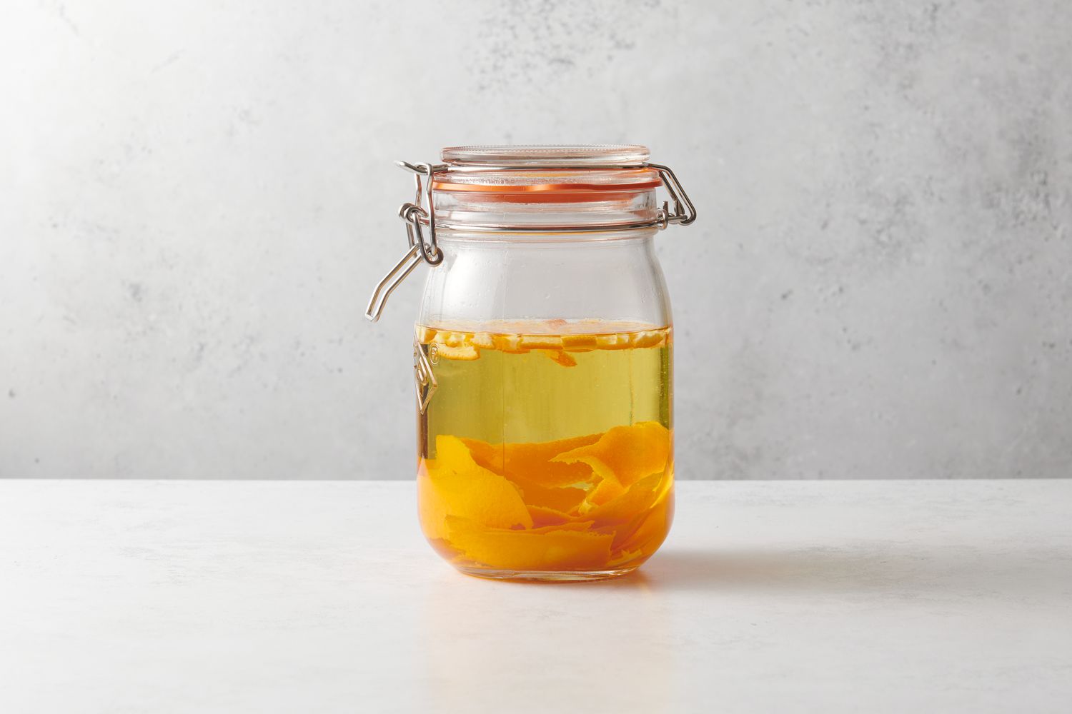 A jar with vodka, orange peels, and dried bitter orange peels