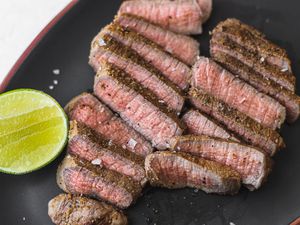 Spiced lime-marinated eye of round steaks on a dark platter with lime