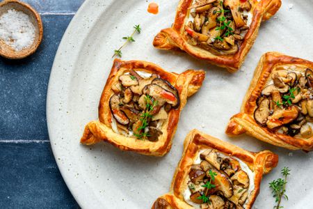 A plate with four mushroom and ricotta puff pastry tarts, with a small bowl of coarse salt