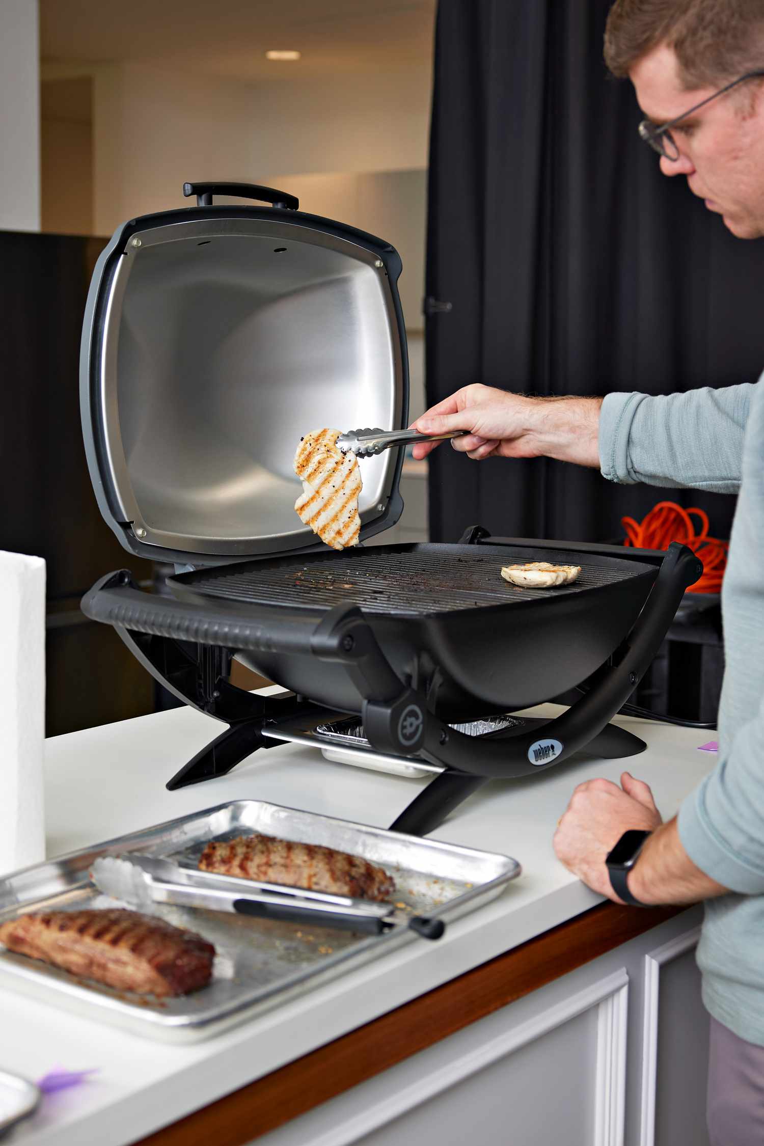 Man using tongs to flip chicken on the Weber Q 1400 Electric Grill