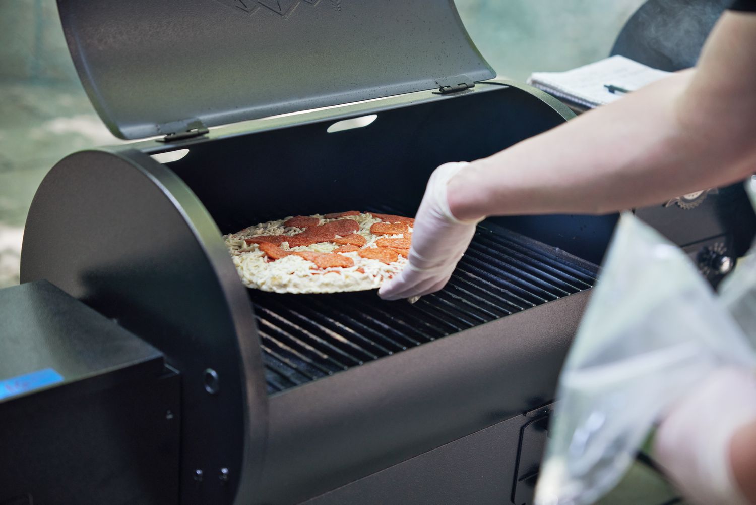 Person placing a pizza on a Traeger TFB30KLF Tailgater Pellet Grill