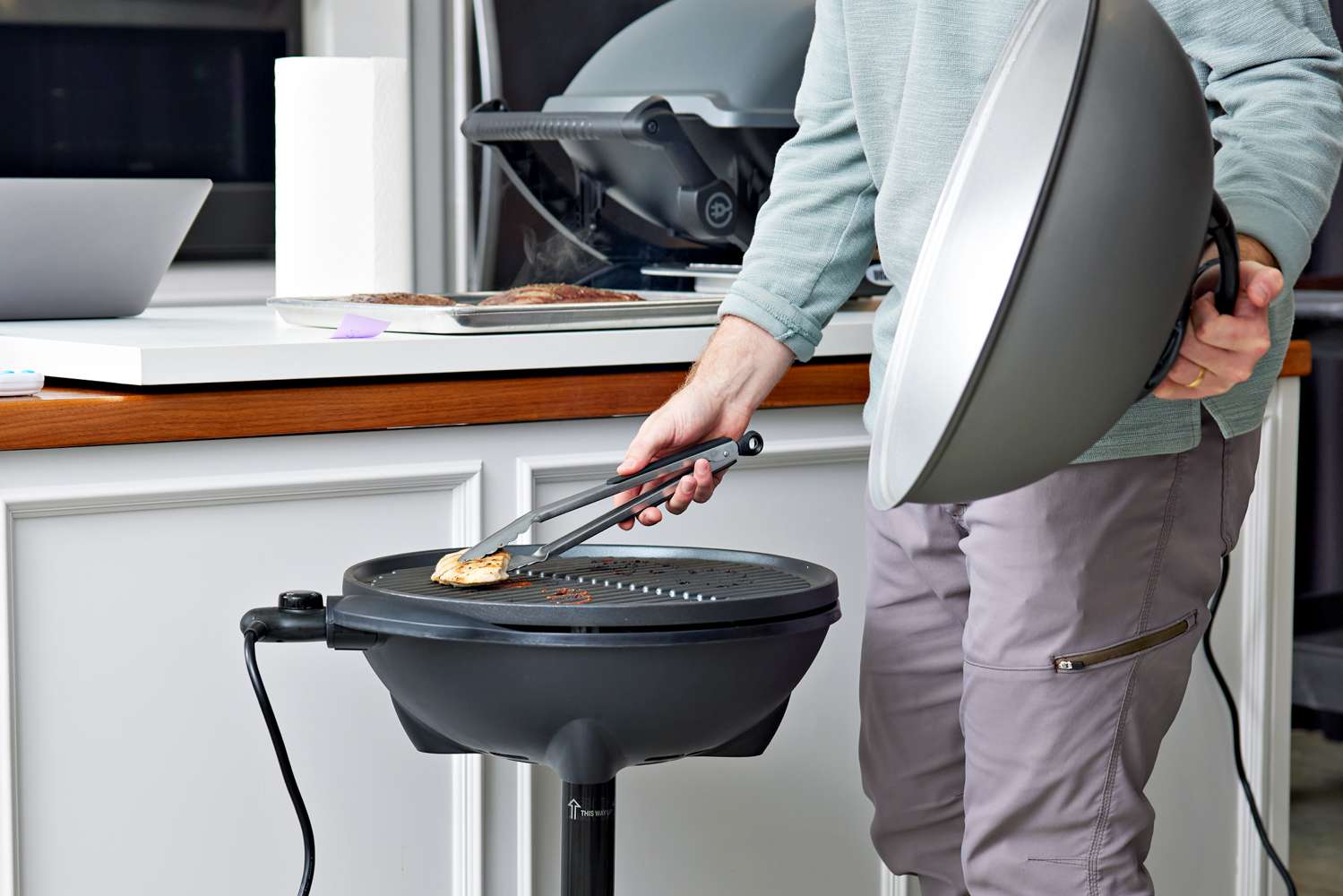 Person flipping chicken with tongs on a George Foreman GFO240S Indoor/Outdoor Electric Grill