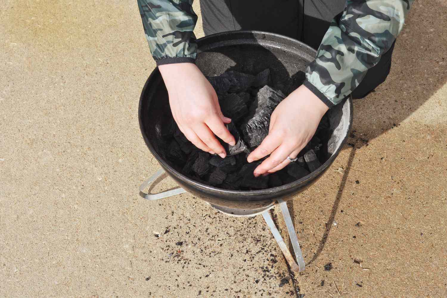 Hands placing Cowboy Hardwood Lump Charcoal into a grill 