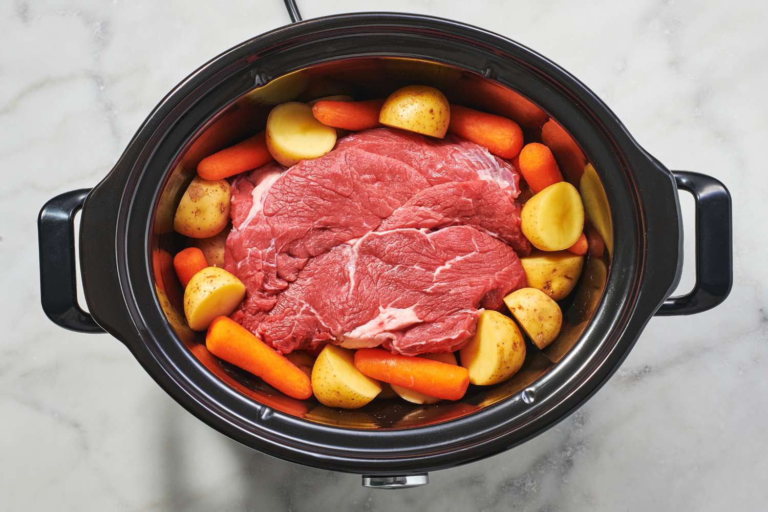 A slow cooker with a beef roast surrounded by carrots and potatoes