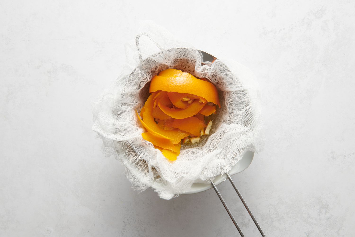 A cheesecloth-lined strainer with orange peels