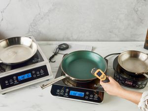 Three induction burners on a counter and a hand measuring temperature