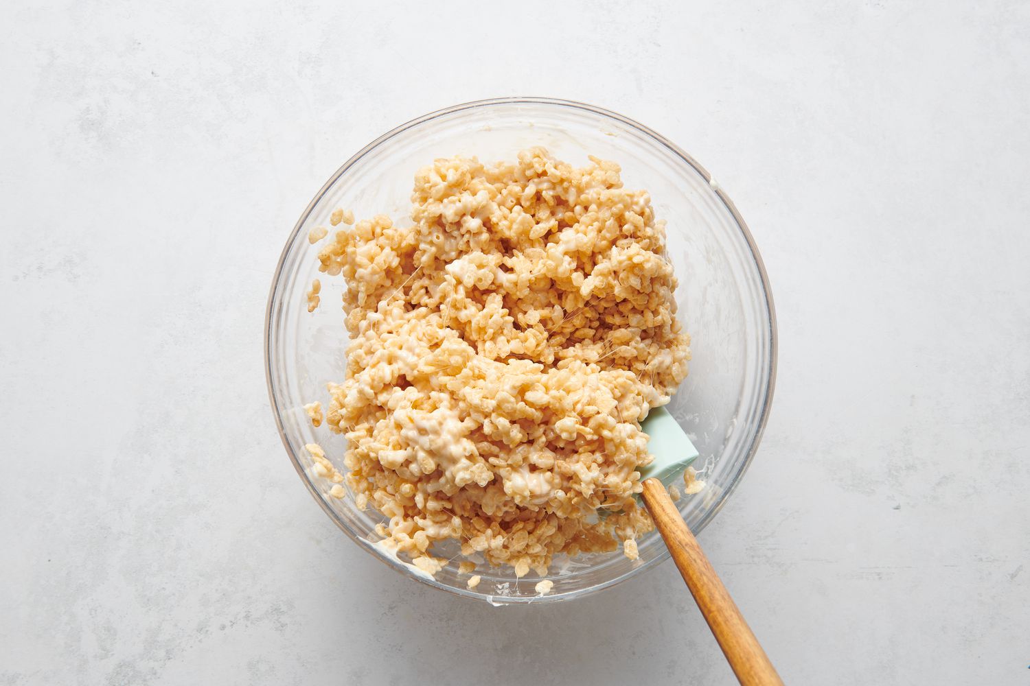 A bowl of puffed rice cereal and melted marshmallows being stirred with a rubber spatula