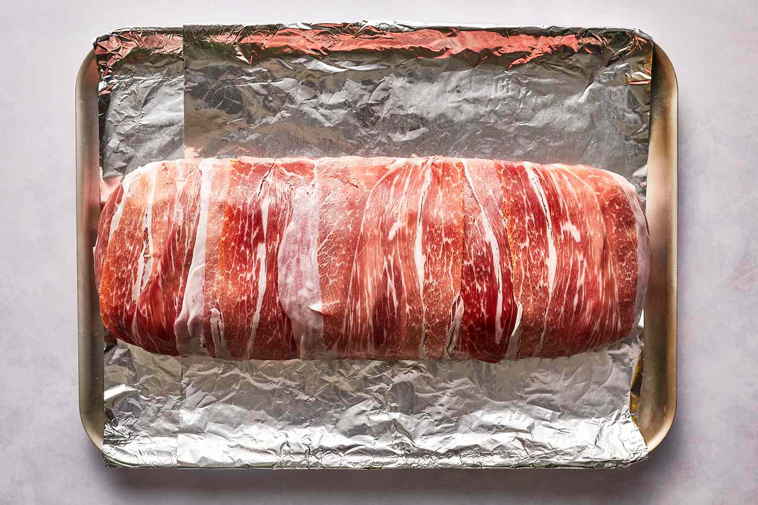 Prosciutto-Wrapped Stuffed Meatloaf on an aluminum foil lined baking sheet 