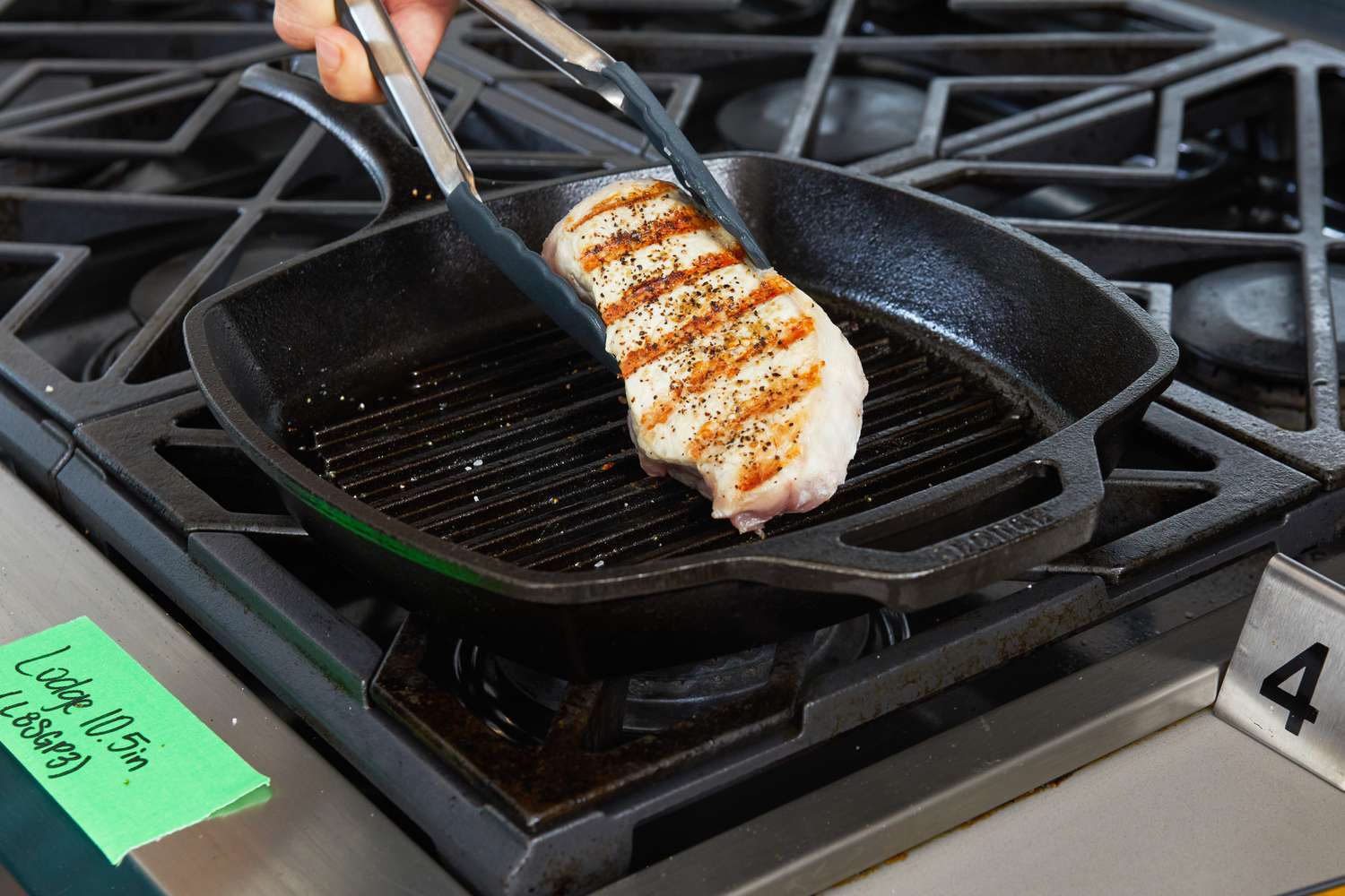 Someone flipping a pork chop that is being cooked using the Lodge Seasoned Cast Iron Square Grill Pan.