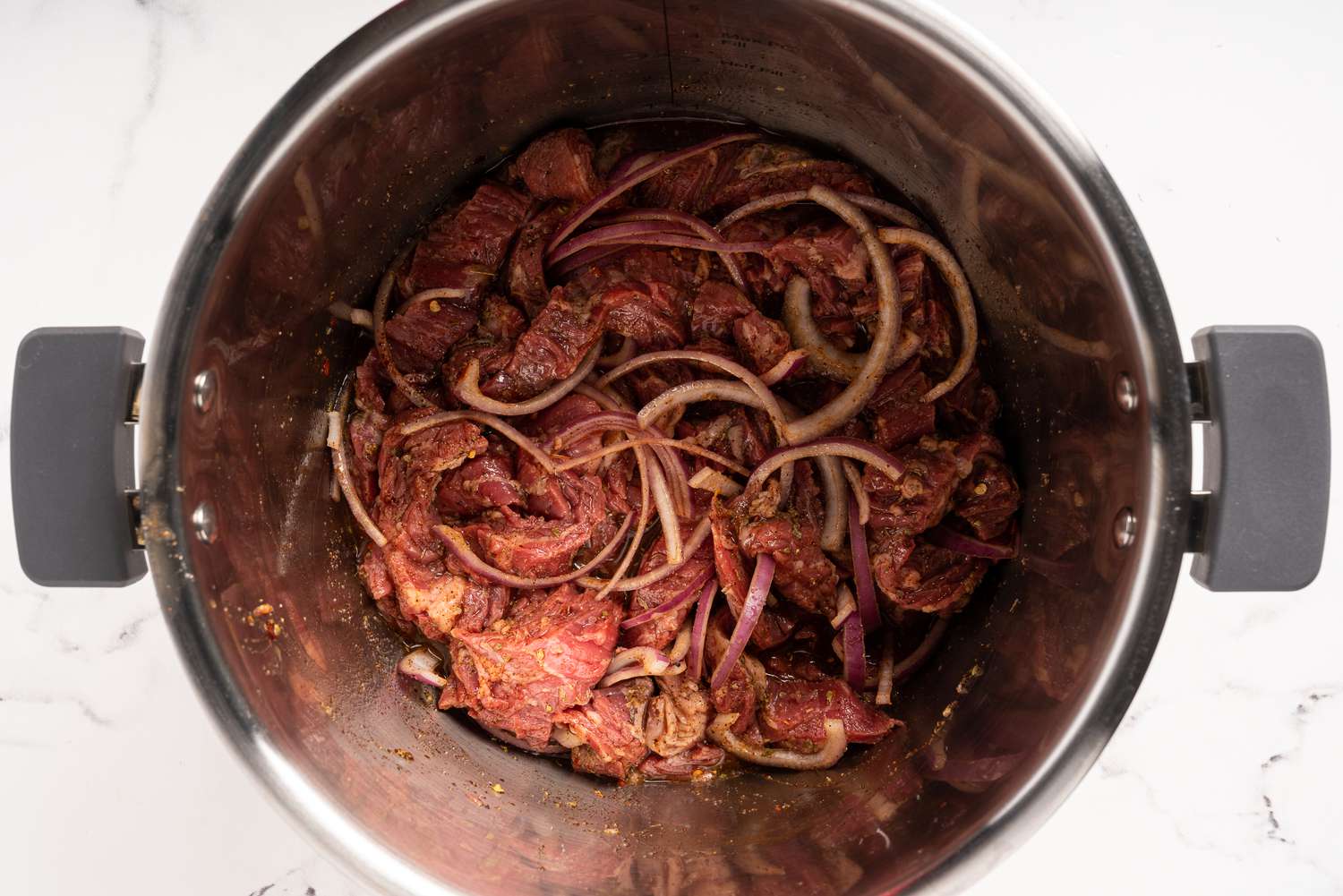 Steak, sliced onion, and seasonings in an Instant Pot 