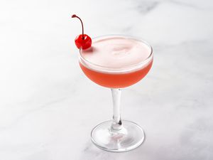 Pink lady cocktail in a glass, garnished with a cherry 