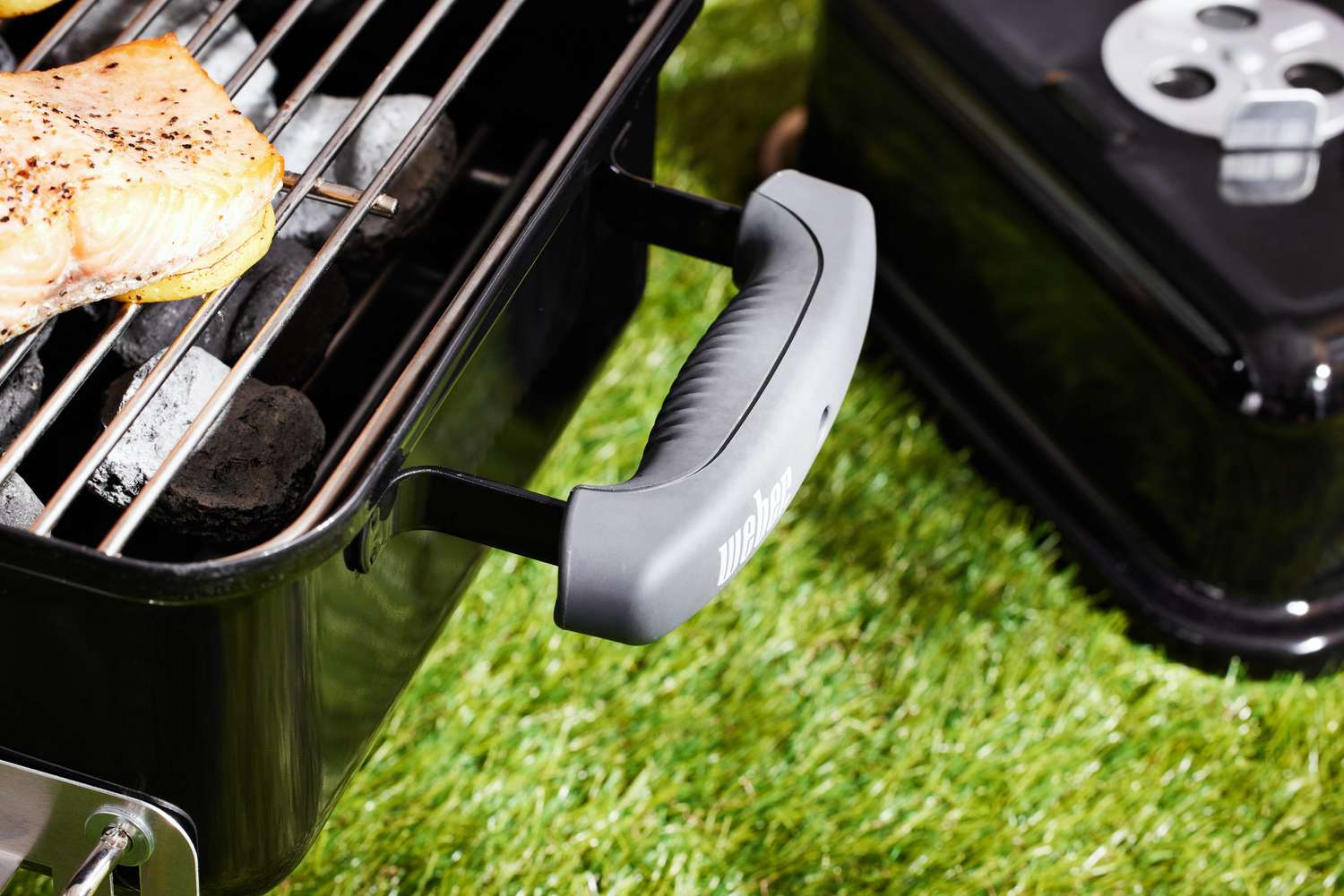 Closeup of the handle of a Weber Go-Anywhere Charcoal Grill that cooking a fillet of salmon 