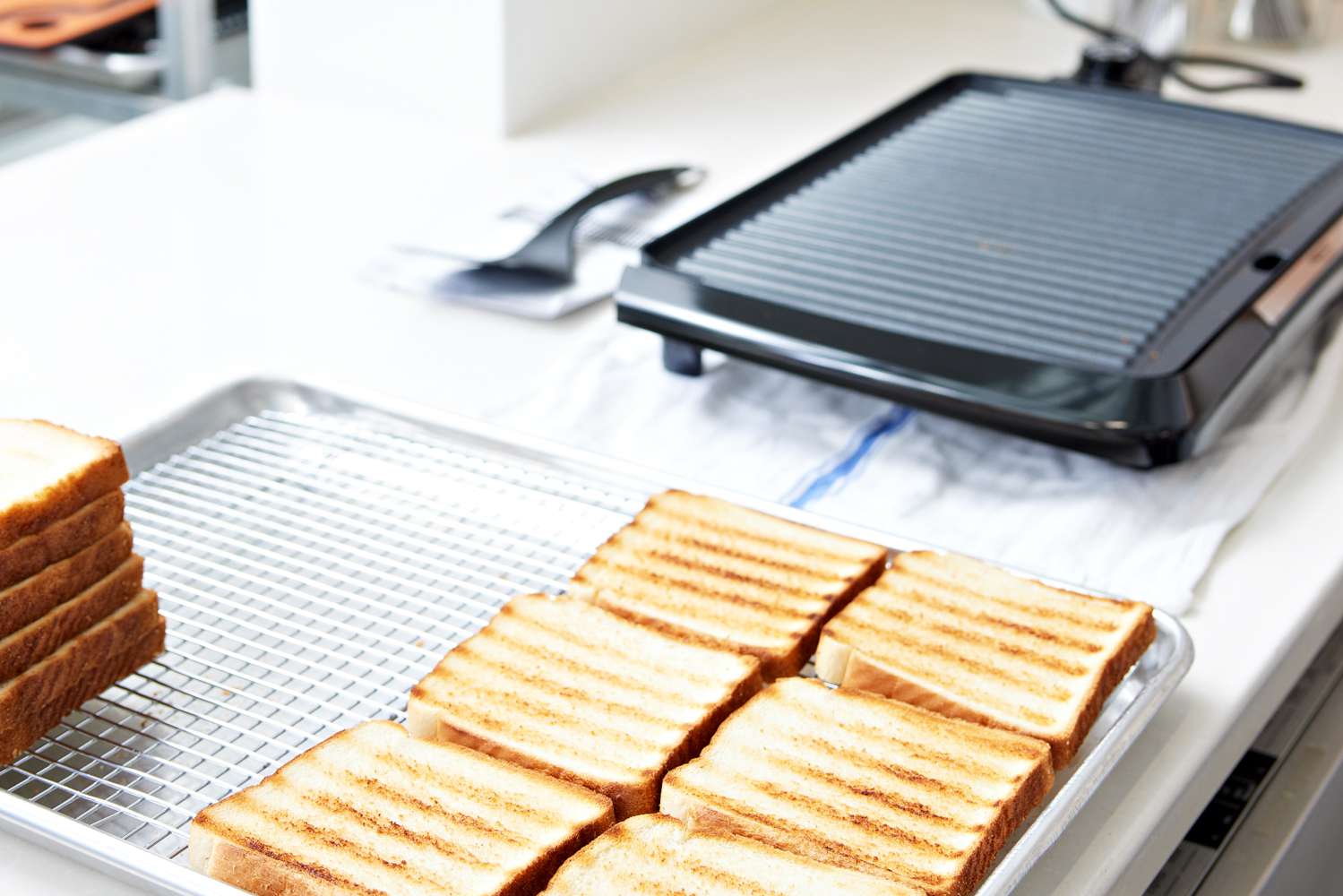 Toasted bread on a cooling rack next to a Presto 09020 Cool Touch Electric Indoor Grill