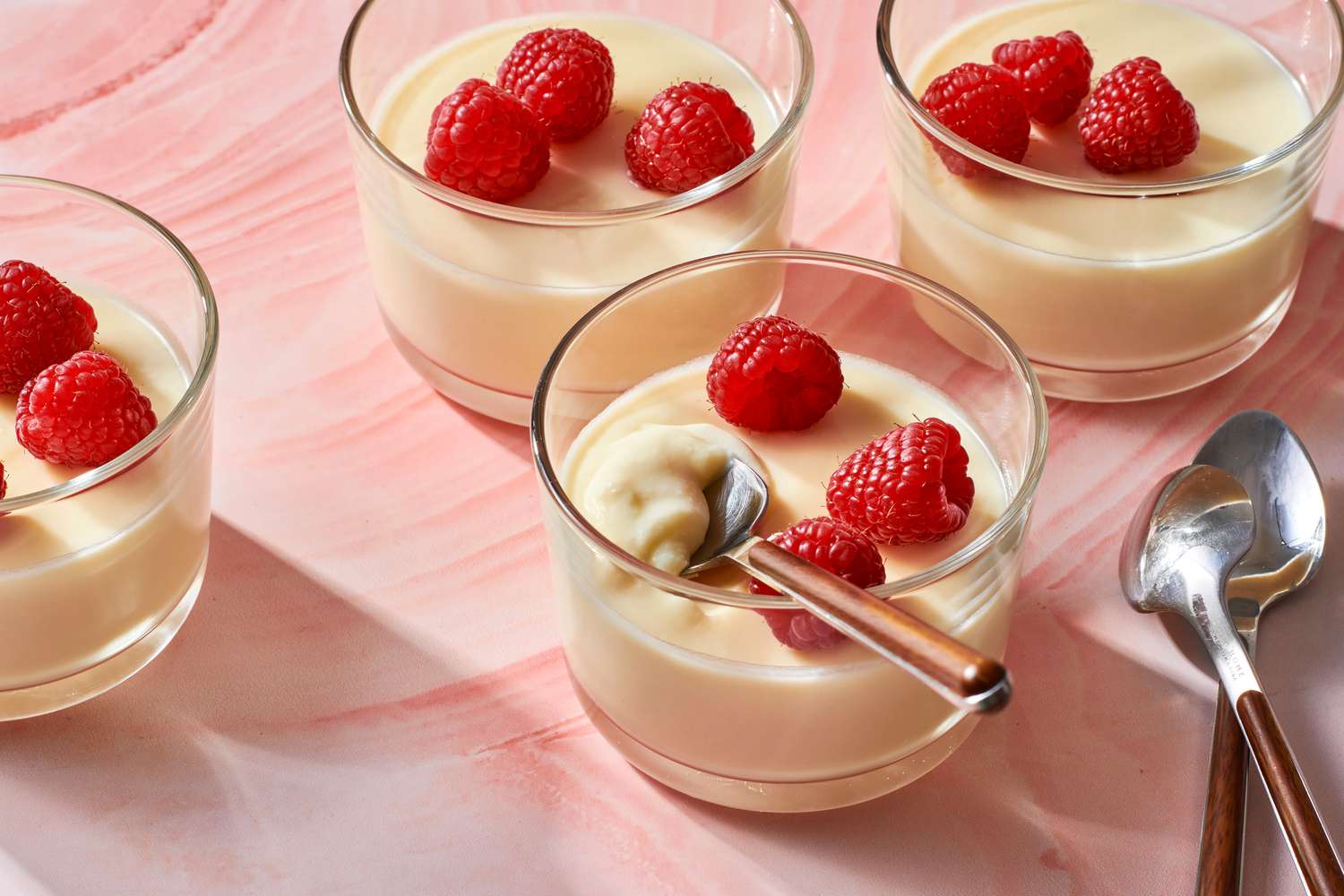 Four glasses of lemon posset topped with fresh raspberries