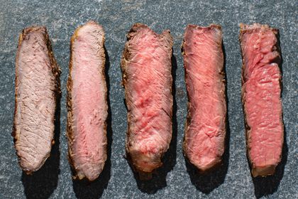 Five pieces of steak ranging from well-done to rare laid out on a slate surface