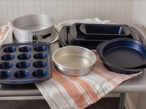 Cake pans, baking sheets, muffin pan, and springform cake pan displayed on table and striped dishcloth