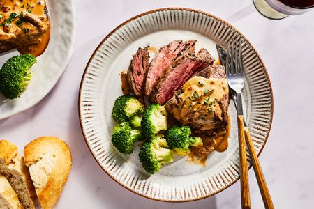 A plate of sliced Steak Diane served with broccoli and bread