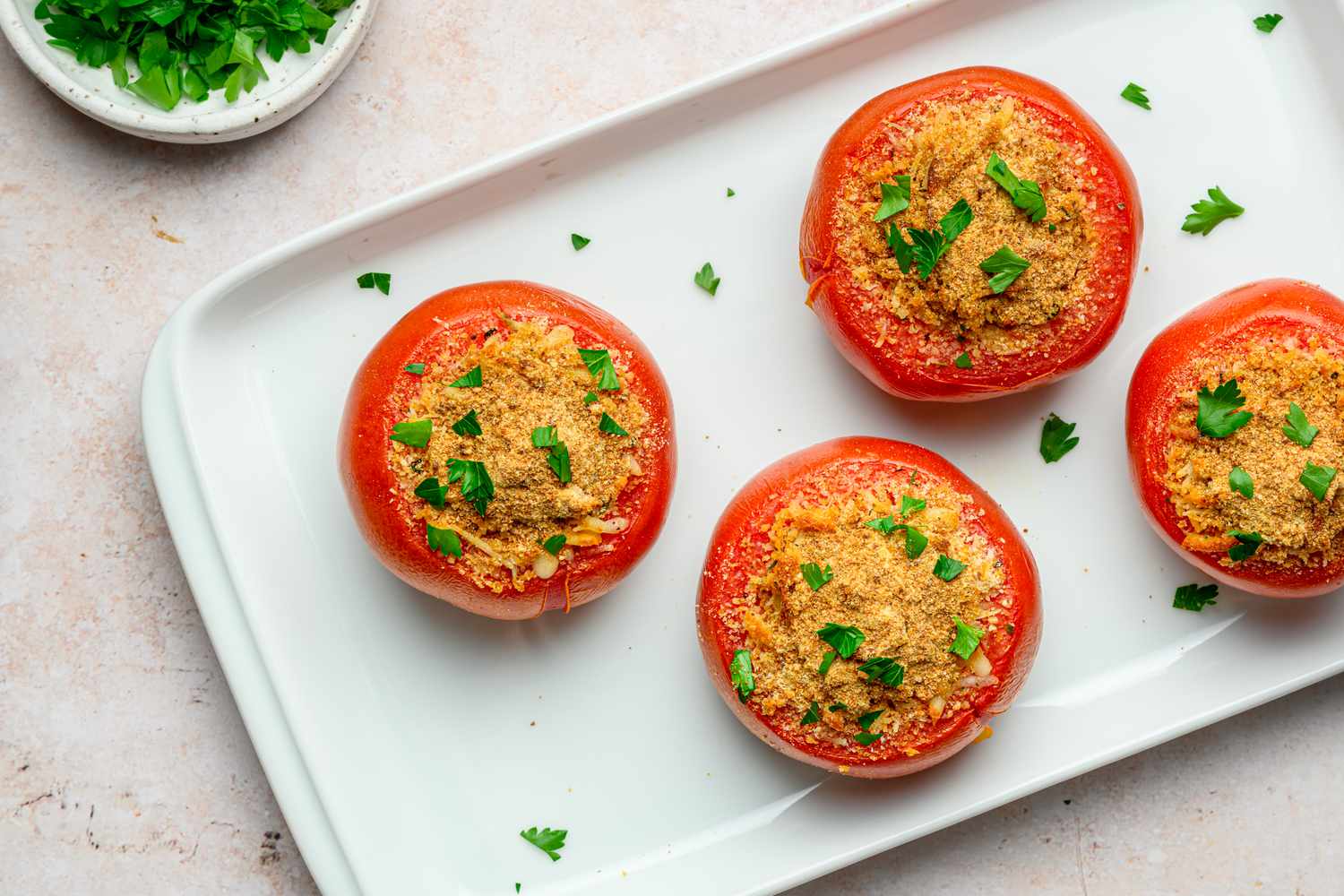 A tray of four stuffed tomatoes topped with chopped parsley
