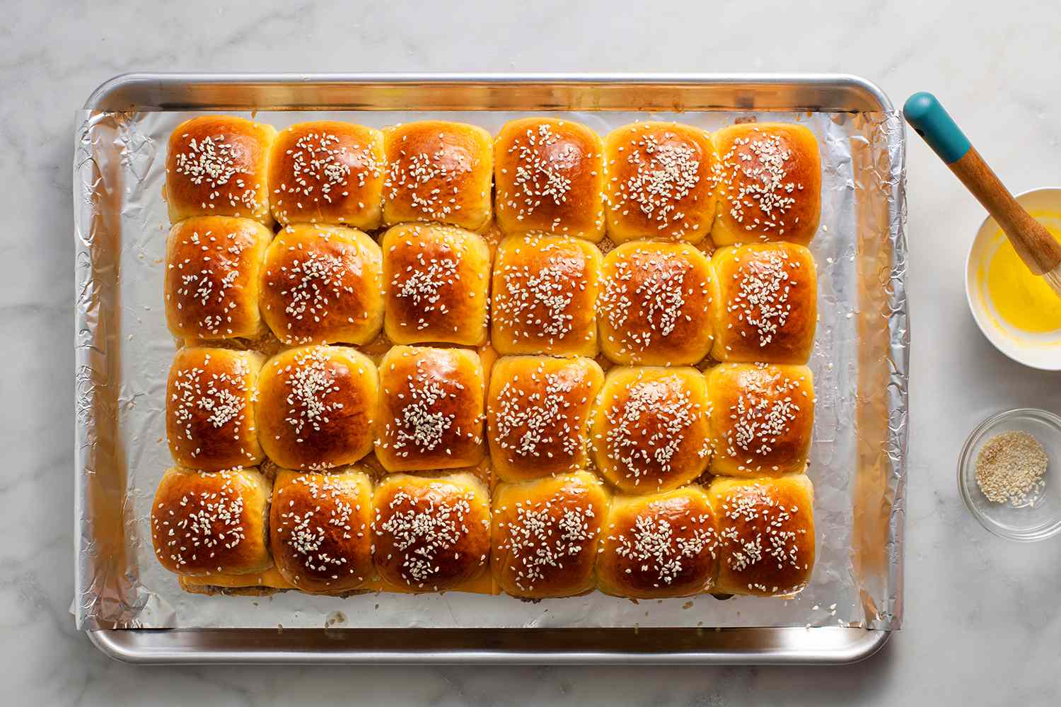 Top roll of buns brushed with butter and sesame seeds