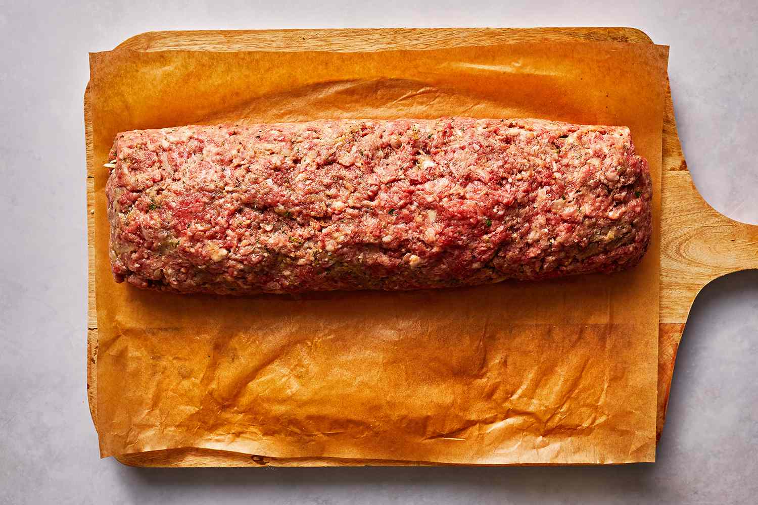 Meatloaf roll on top of a parchment paper lined cutting board 