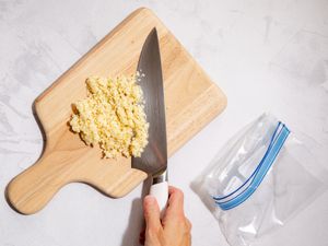 A cutting board with a bunch of minced garlic next to a plastic bag.