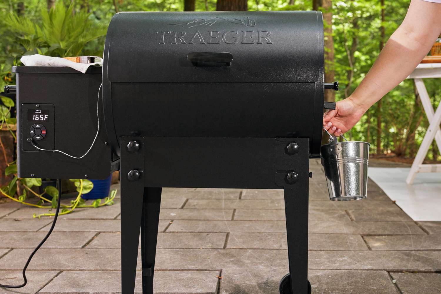 Hand lifting a small bucket from the side of a Traeger TFB30KLF Tailgater Pellet Grill