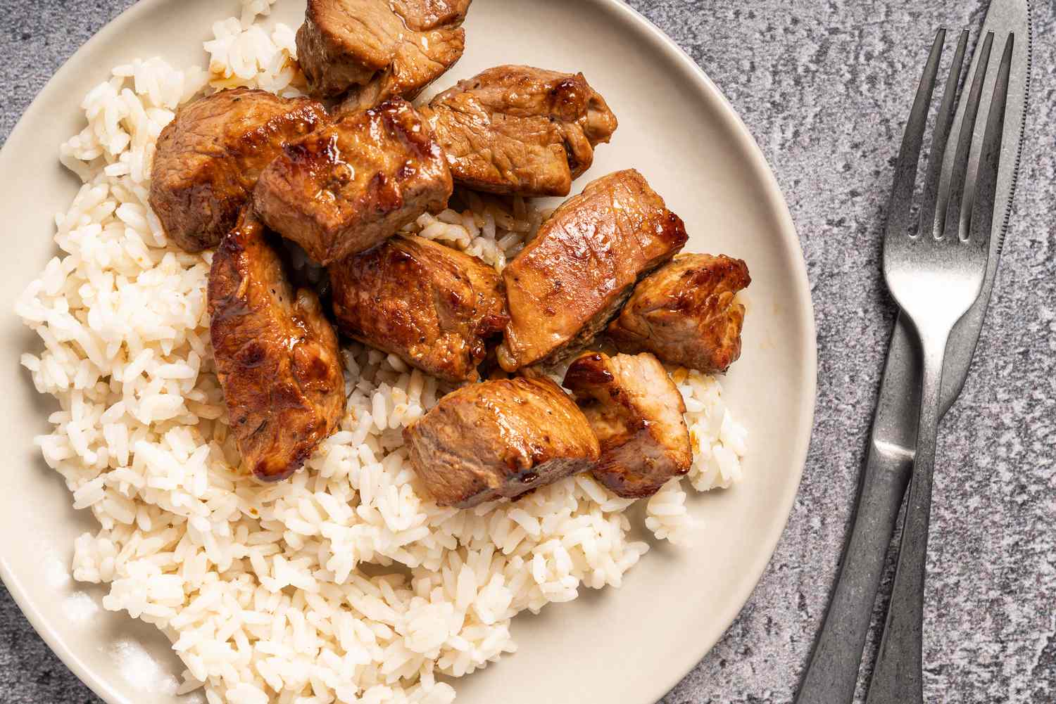 Browned stir-fried pork cubes with rice on a dinner plate