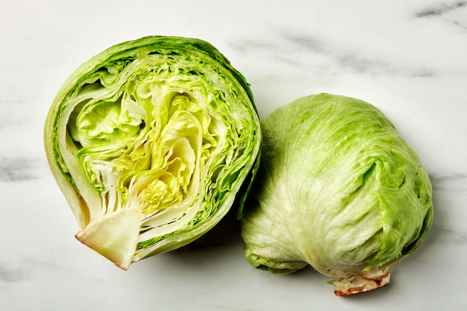 A head of iceberg lettuce, cut in half, on a marble surface