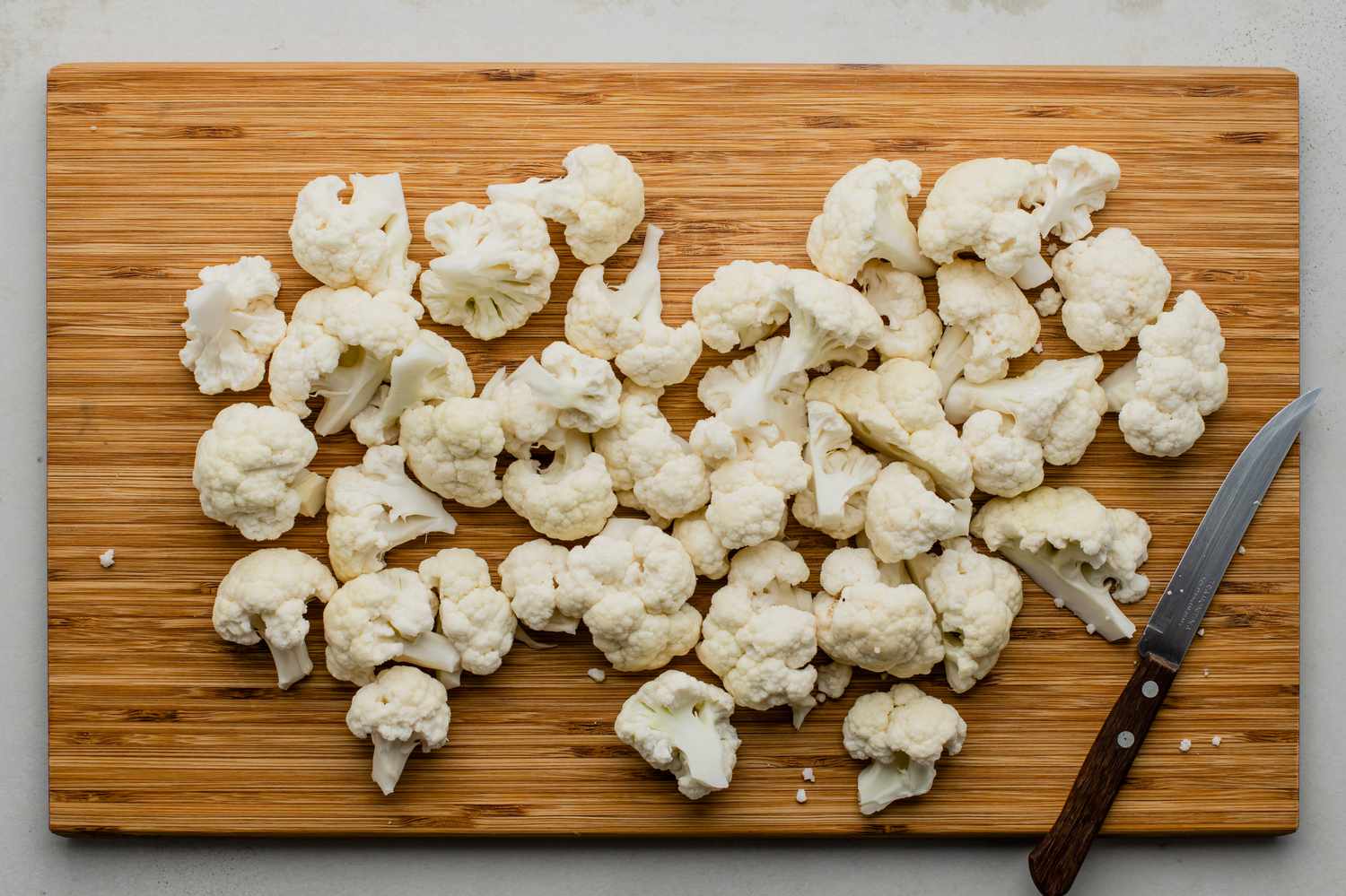 Cauliflower cut into florets on a wooden cutting board