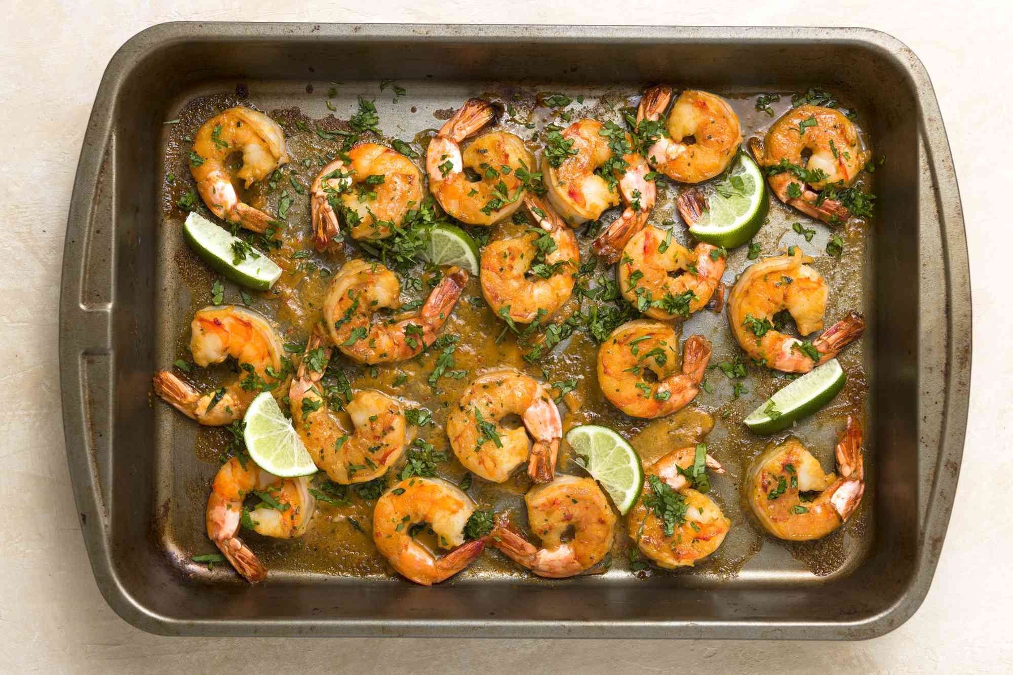 A baking sheet with cooked shrimp, lime wedges, and cilantro